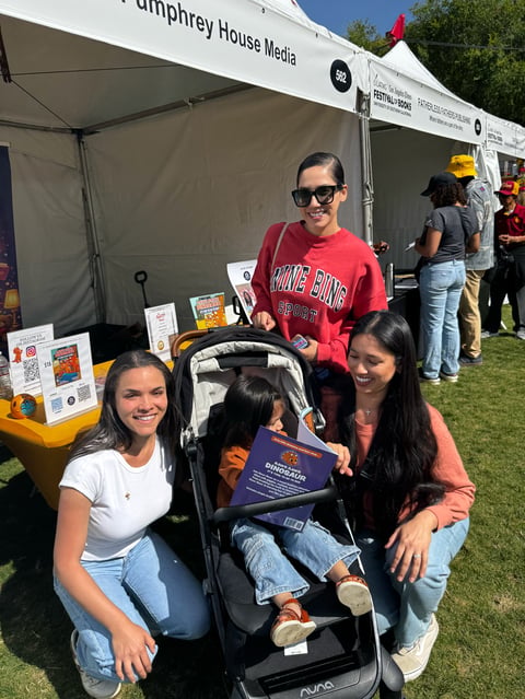 Group of people posing at Humphrey House Media tent booth at outdoor event with child in stroller