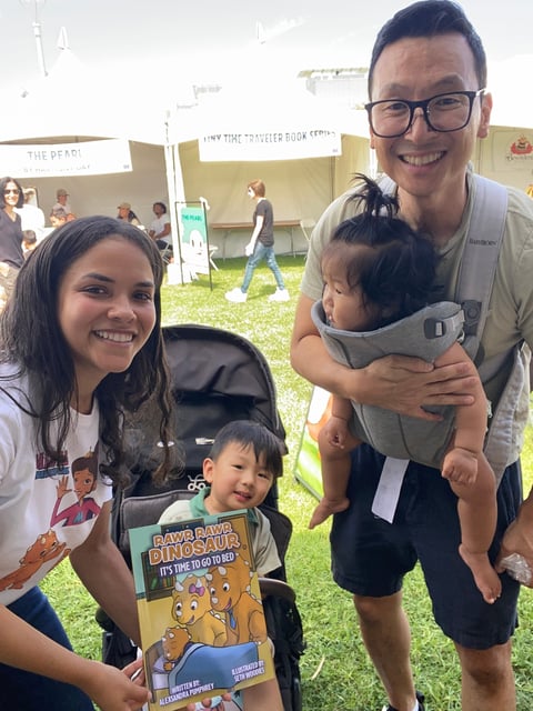 Family of four smiling at an outdoor event with tents and grass in the background
