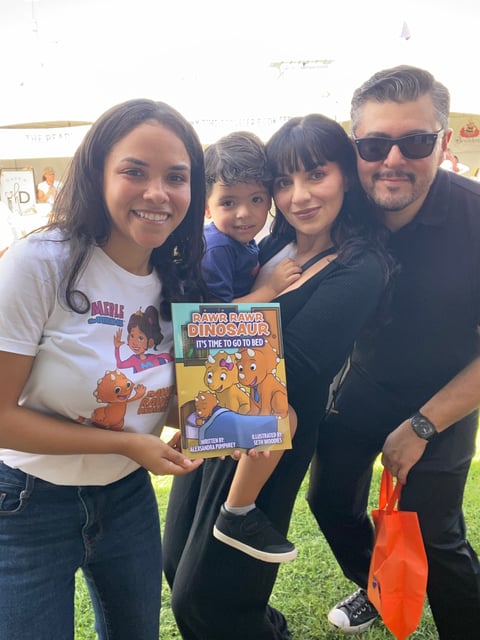 Family of four smiling outdoors while holding a Dave and Dinosaur childrens book