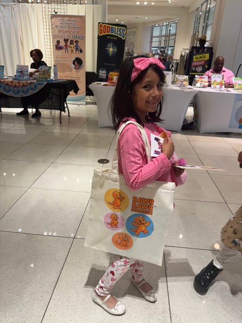Young girl wearing pink holding a tote bag with decorated badges at an indoor event or convention