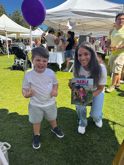 Young child and teenager smiling at outdoor festival holding purple balloon and comic book