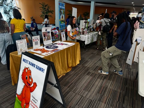 Community event with vendor booths displaying merchandise and artwork behind gold tablecloths in an indoor convention-style space