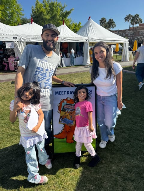Family of four posing with cardboard cutout at outdoor festival with white tents and green grass