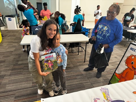 Woman and young child posing together at a community event with other people and activity stations in the background