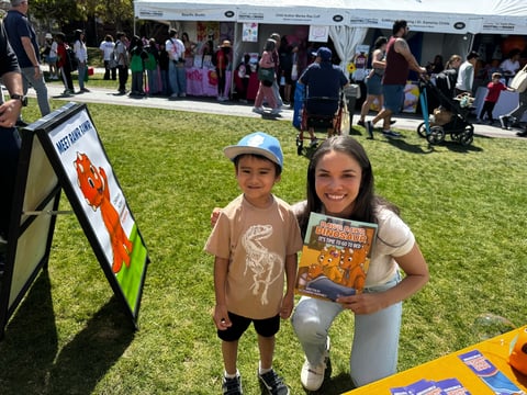 Young boy and girl smiling at outdoor event on grass with tents and crowds in background