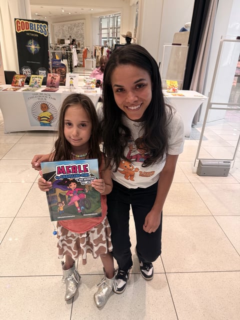 Two young girls smiling at camera in a retail store, holding a Merle magazine, wearing casual clothing